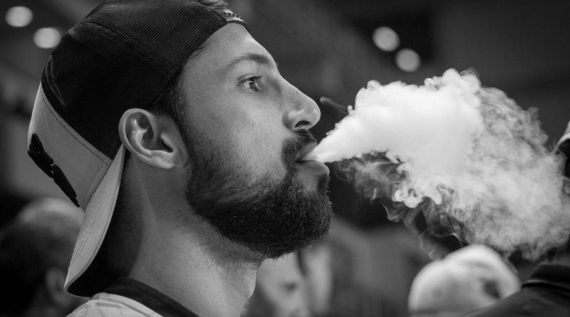 grayscale photography of man wearing cap with smoke on mouth
